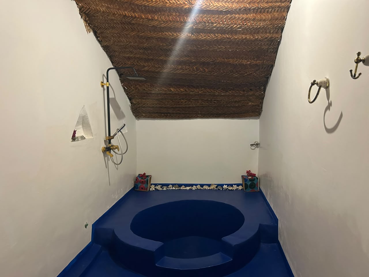 Bathroom inside the Makuti Banda with woven palm ceiling and sunken blue floor
